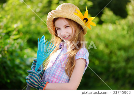 Adorable little girl wearing straw hat holding garden tools Adorable little girl wearing straw hat holding garden tools 33745903