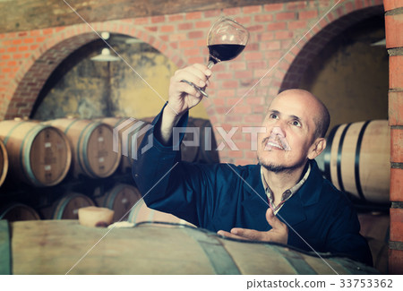 winery worker with glass of wine in cellar. 33753362