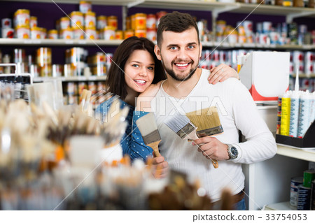 Couple deciding on brush for decorating house in paint supplies store Couple deciding on brush for decorating house in paint supplies store 33754053
