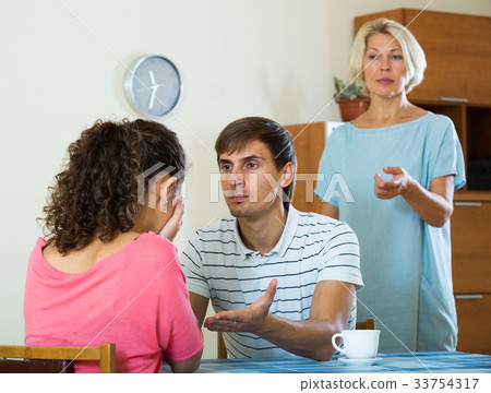 Upset female retiree watching adult kids quarrelling at home Upset female retiree watching adult kids quarrelling at home 33754317