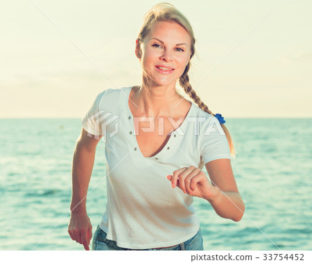 Smiling adult woman in white T-shirt is jogging on the beach Smiling adult woman in white T-shirt is jogging on the beach 33754452