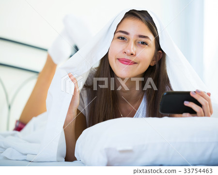 Smiling girl with smartphone hiding in bed Smiling girl with smartphone hiding in bed 33754463