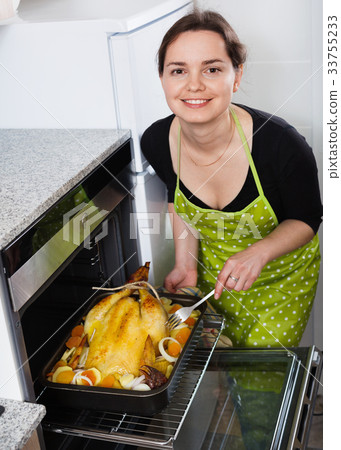 Young cheerful woman roasting cockerel for dinner Young cheerful woman roasting cockerel for dinner 33755233