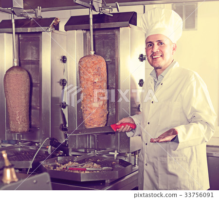 man chef wearing uniform cutting meat for kebab on kitchen in fa man chef wearing uniform cutting meat for kebab on kitchen in fa 33756091