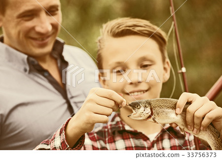 Man with teenager boy releasing fish from hook Man with teenager boy releasing fish from hook 33756373