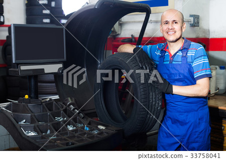 Mature male technician holding car wheel ready to work with balancing machinery at workshop Mature male technician holding car wheel ready to work with balancing machinery at workshop 33758041