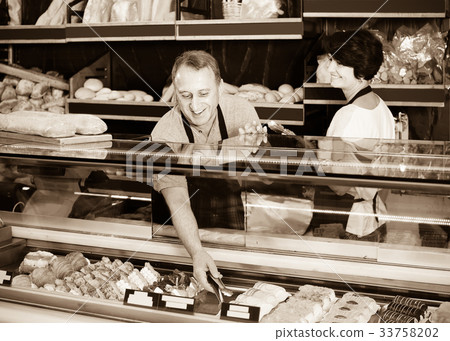 staff offering fresh baguettes and buns in bakery 33758202