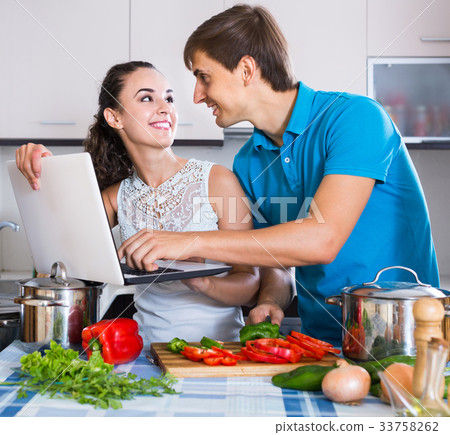 couple with vegetables and laptop in domestic kitchen 33758262