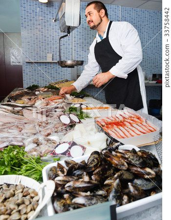 Seller in black apron shows fish counter 33758442