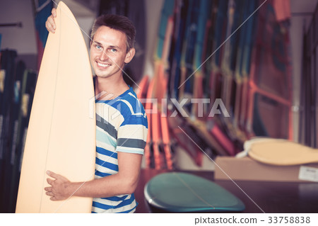 male is posing with surfboard in store on the beach. male is posing with surfboard in store on the beach. 33758838