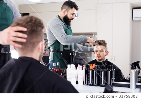 Young male stylist creating haircut for man client at hairdressing salon Young male stylist creating haircut for man client at hairdressing salon 33759308