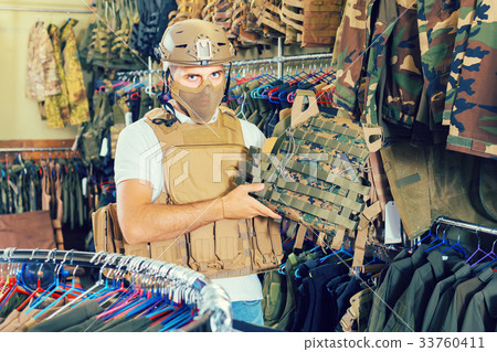 Young guy choosing flak jacket in military shop 33760411