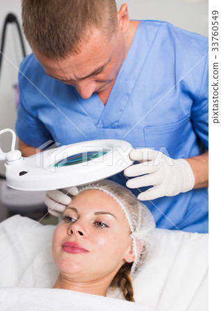 Specialist is analysing skin of female patient with using magnification before the procedure Specialist is analysing skin of female patient with using magnification before the procedure 33760549