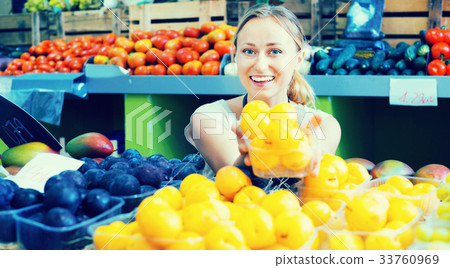 Cheerful female seller wearing apron holding plums 33760969