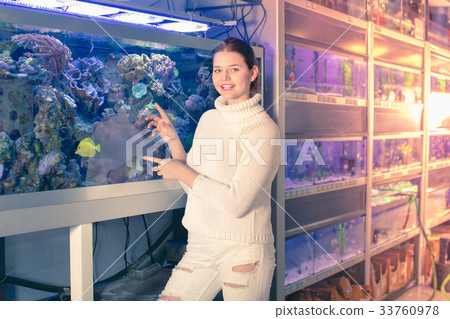 Girl in aquarium shop with interest looking at colorful fishes Girl in aquarium shop with interest looking at colorful fishes 33760978
