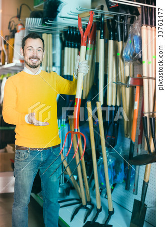 Smiling guy deciding on best hayfork in garden equipment shop Smiling guy deciding on best hayfork in garden equipment shop 33761477