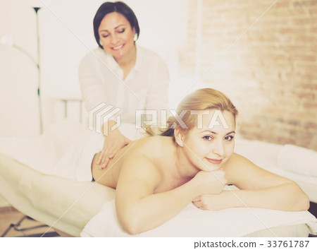 Mature massagist is doing massage of back and loin to smiling young woman Mature massagist is doing massage of back and loin to smiling young woman 33761787