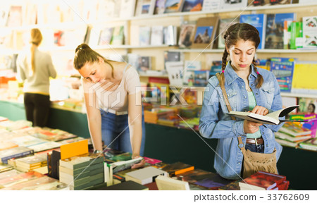 glad woman showing open book to smiling girl in book boutique glad woman showing open book to smiling girl in book boutique 33762609