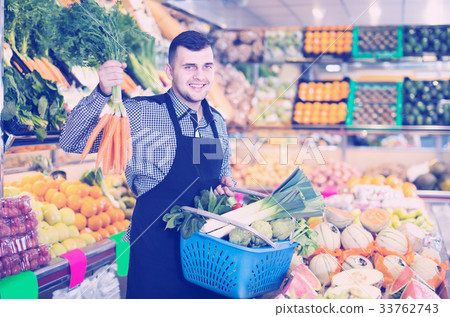 young male seller assisting in buying fruit and vegetables in grocery shop young male seller assisting in buying fruit and vegetables in grocery shop 33762743