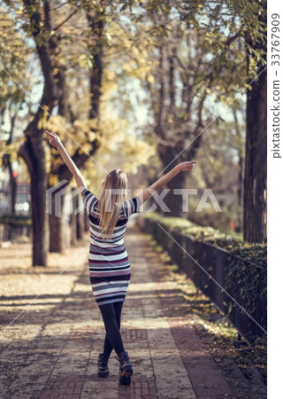 Young blonde woman walking in the street raising her arms Young blonde woman walking in the street raising her arms 33767909