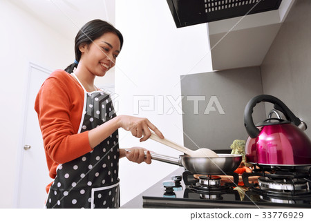 Smiling asian woman using frying pan and cooking 33776929