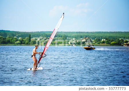Windsurfer on board with a white sail floating Windsurfer on board with a white sail floating 33777773