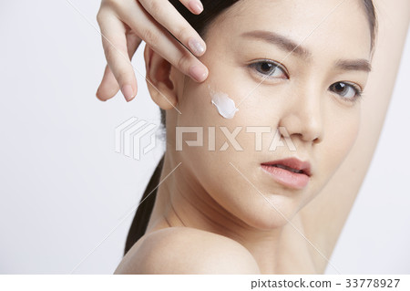 a girl is applying cream on her face and looking at something a girl is applying cream on her face and looking at something 33778927