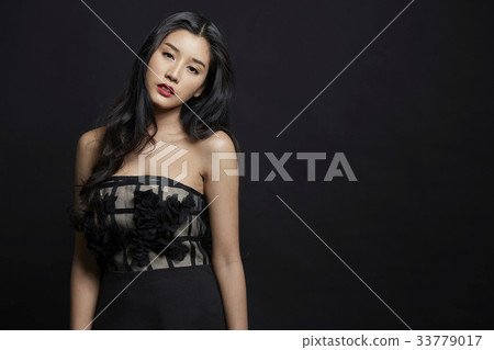 attractive female model in black dress is standing and posing on black background attractive female model in black dress is standing and posing on black background 33779017