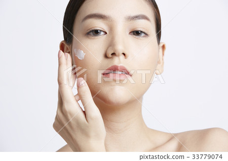 portrait of woman applying cream and looking at camera 33779074