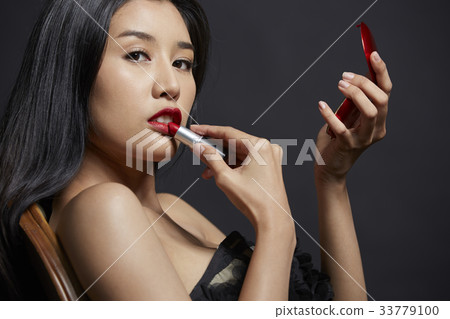 beautiful woman is sitting and applying lipstick 33779100