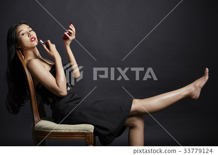 An Asian girl with a long black hair is sitting and making up on black background An Asian girl with a long black hair is sitting and making up on black background 33779124