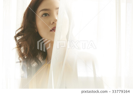 A beautiful Thai girl is standing and looking at something beside the white curtain A beautiful Thai girl is standing and looking at something beside the white curtain 33779164