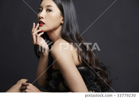 The picture of girl sitting and putting the fingers on her lips on black background 33779230