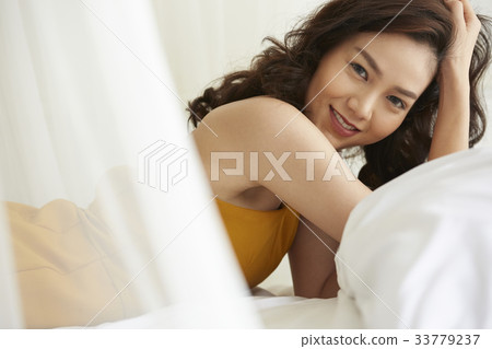 The picture of a happy woman laying down on a bed and posing 33779237