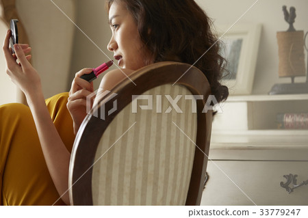 An Asian young woman is sitting on the chair and using the lipstick. An Asian young woman is sitting on the chair and using the lipstick. 33779247