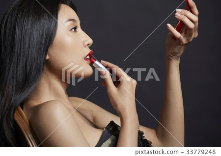 An elegant woman is leaning on the chair and looking at the hand mirror. An elegant woman is leaning on the chair and looking at the hand mirror. 33779248