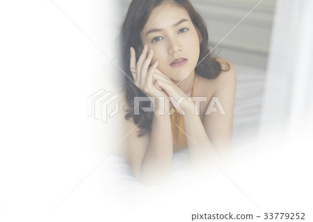 portrait of an Asian young woman staring through the glass while lying on the bed. portrait of an Asian young woman staring through the glass while lying on the bed. 33779252