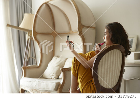 portrait of beautiful woman sitting on a chair and making up inside. 33779273