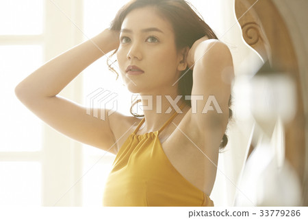 An Asian young woman is touching her hair and looking at something 33779286