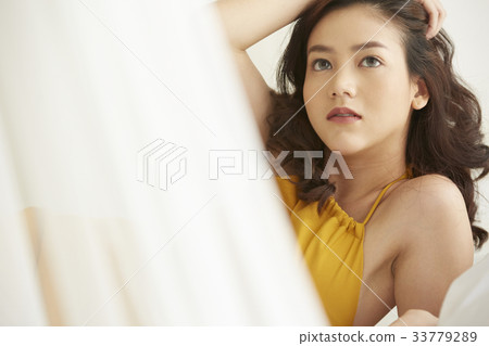 An Asian young woman is looking at something while posing on bed. 33779289