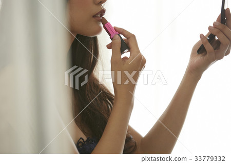 photo of a woman holding a lipstick and making up herself. 33779332