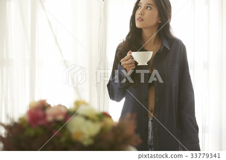 Asian beautiful woman holding a cup of morning cofee in her room Asian beautiful woman holding a cup of morning cofee in her room 33779341