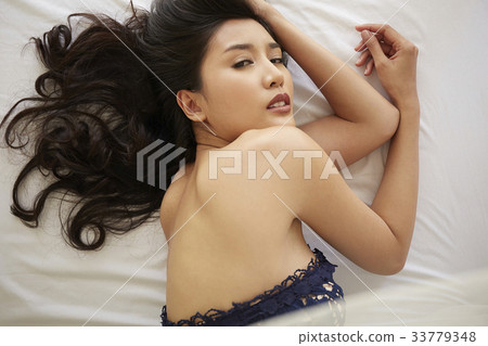 photo of a woman lying on a bed and looking at camera. 33779348