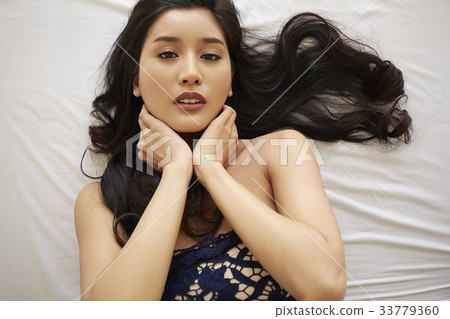 photo of a woman holding her neck while lying on a bed. 33779360
