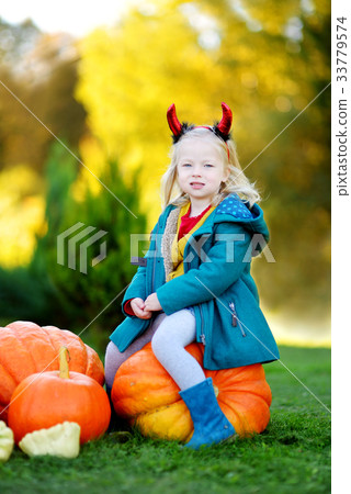 Adorable little girl wearing halloween costume having fun on a pumpkin patch 33779574