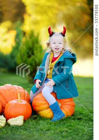 Adorable little girl wearing halloween costume having fun on a pumpkin patch Adorable little girl wearing halloween costume having fun on a pumpkin patch 33779588