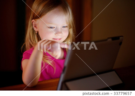 Adorable girl playing with a digital tablet in a dark room Adorable girl playing with a digital tablet in a dark room 33779657