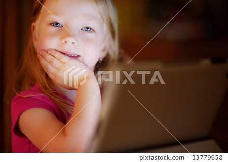 Adorable girl playing with a digital tablet in a dark room Adorable girl playing with a digital tablet in a dark room 33779658
