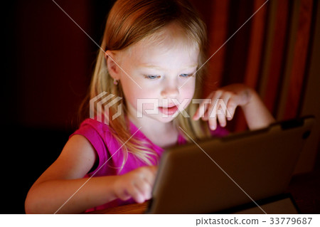Adorable girl playing with a digital tablet in a dark room 33779687