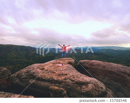 Man hiker on sharp cliff. Hiker climbed up to peak Man hiker on sharp cliff. Hiker climbed up to peak 33788546